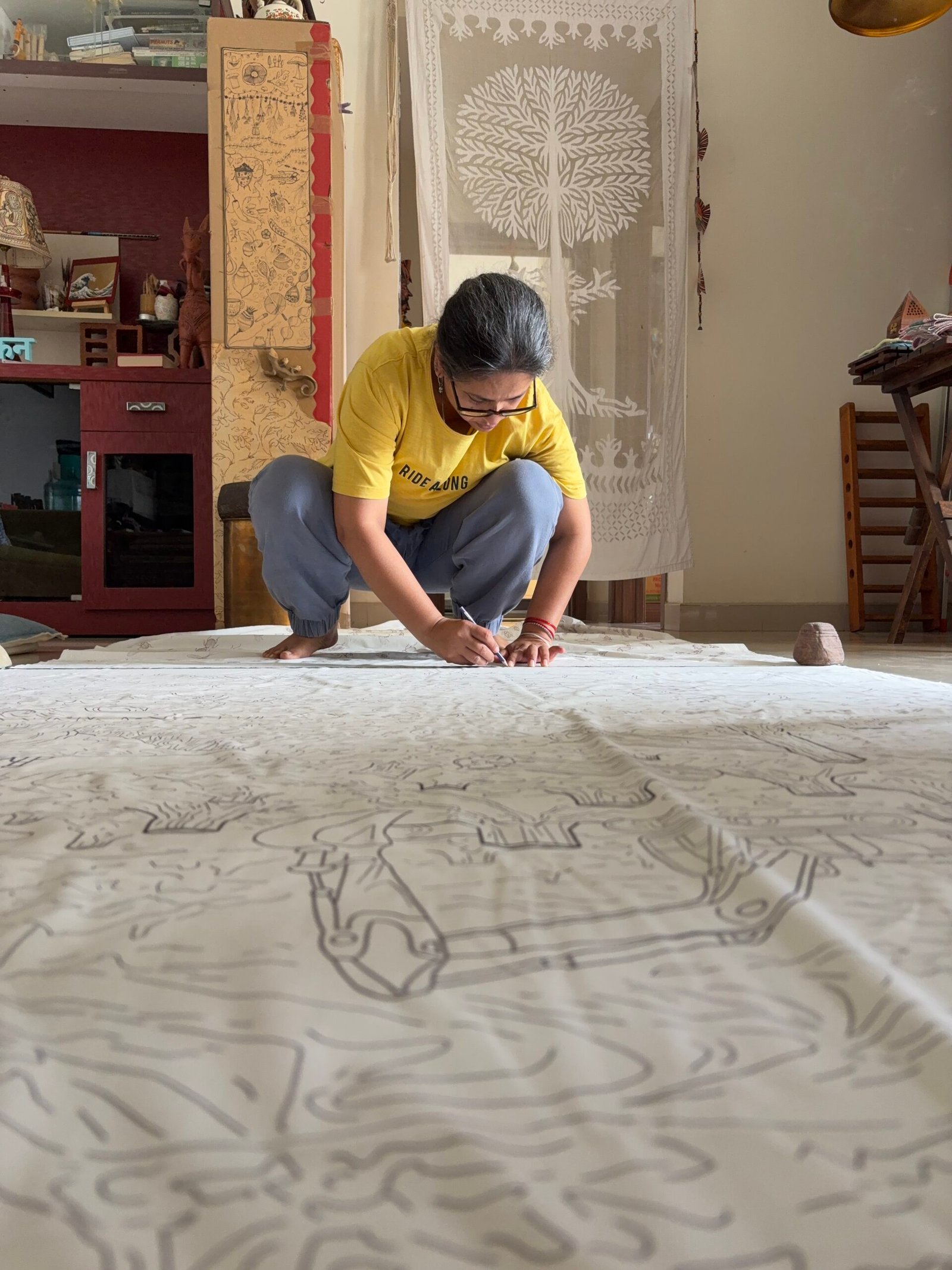 Designer Meghana Singh sitting hunched over a large piece of cloth, working on her climate movement and data piece.