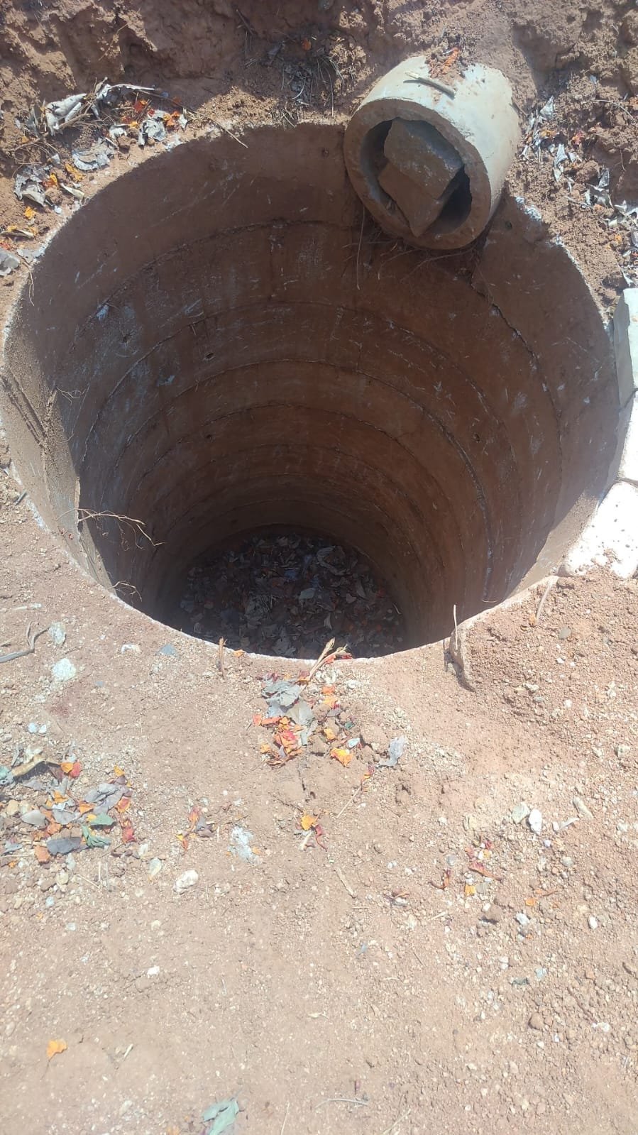 A rainwater harvesting recharge pit, silted and filled with debris. Nobody came back to desilt it. With large stones obstructing the rainwater inlet pipe.